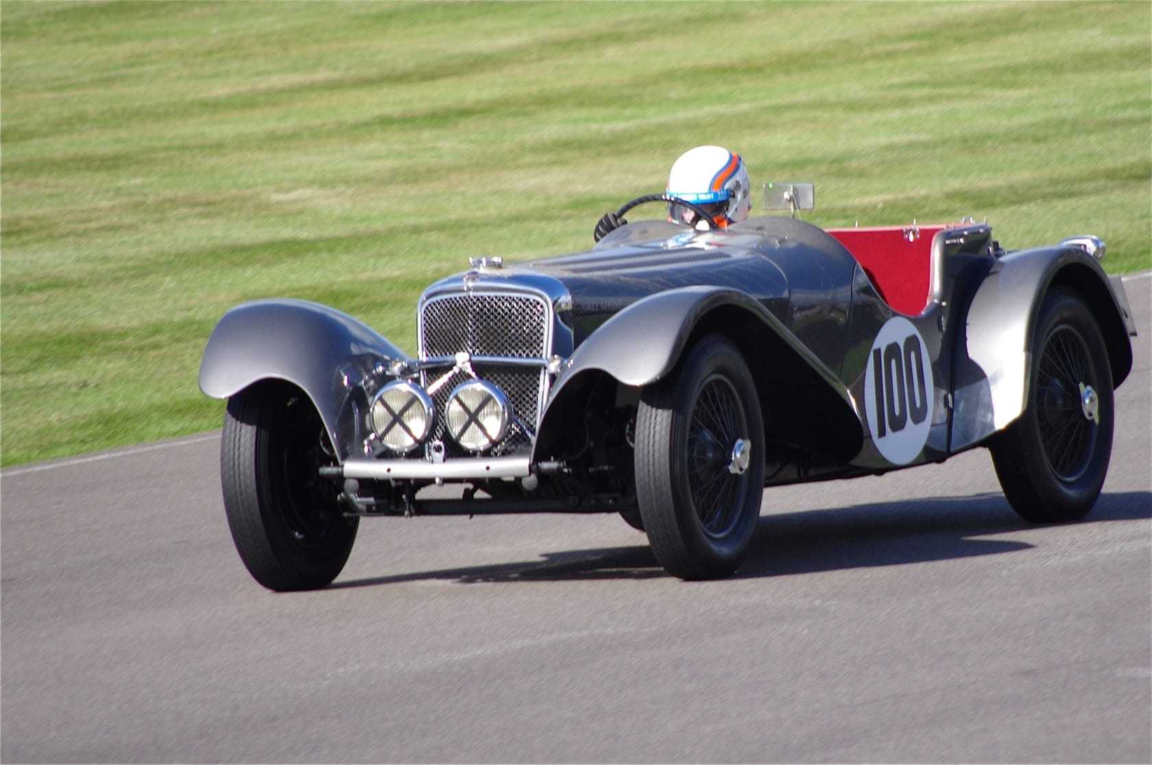 A silver SS Jaguar 100 racing on a circuit, front three-quarter view, race number 100