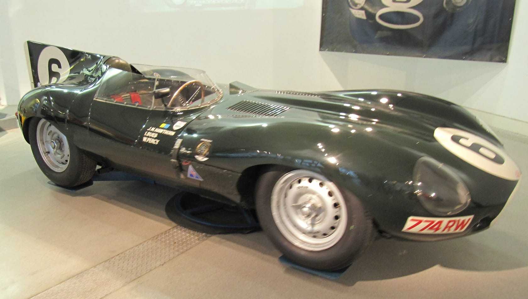 A dark green 1955 Jaguar D-Type with the number 6 displayed in a museum, registration 774 RW
