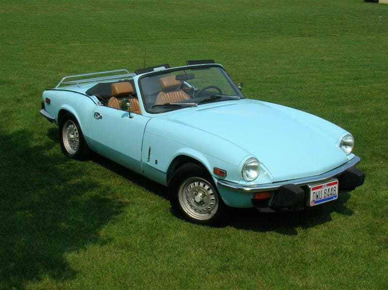 A pale blue Triumph Spitfire 1500 with the top down, front three-quarter view on grass