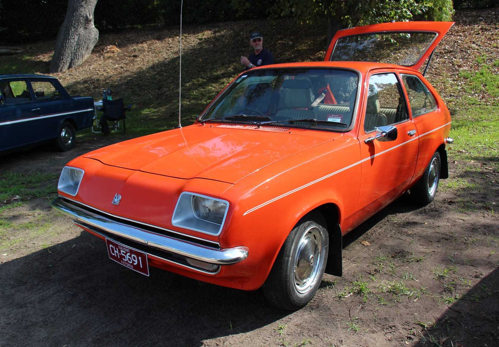 A bright orange 1979 Vauxhall Chevette three-door hatchback at an outdoor classic car show, front three-quarter view showing the shovel-nose grille