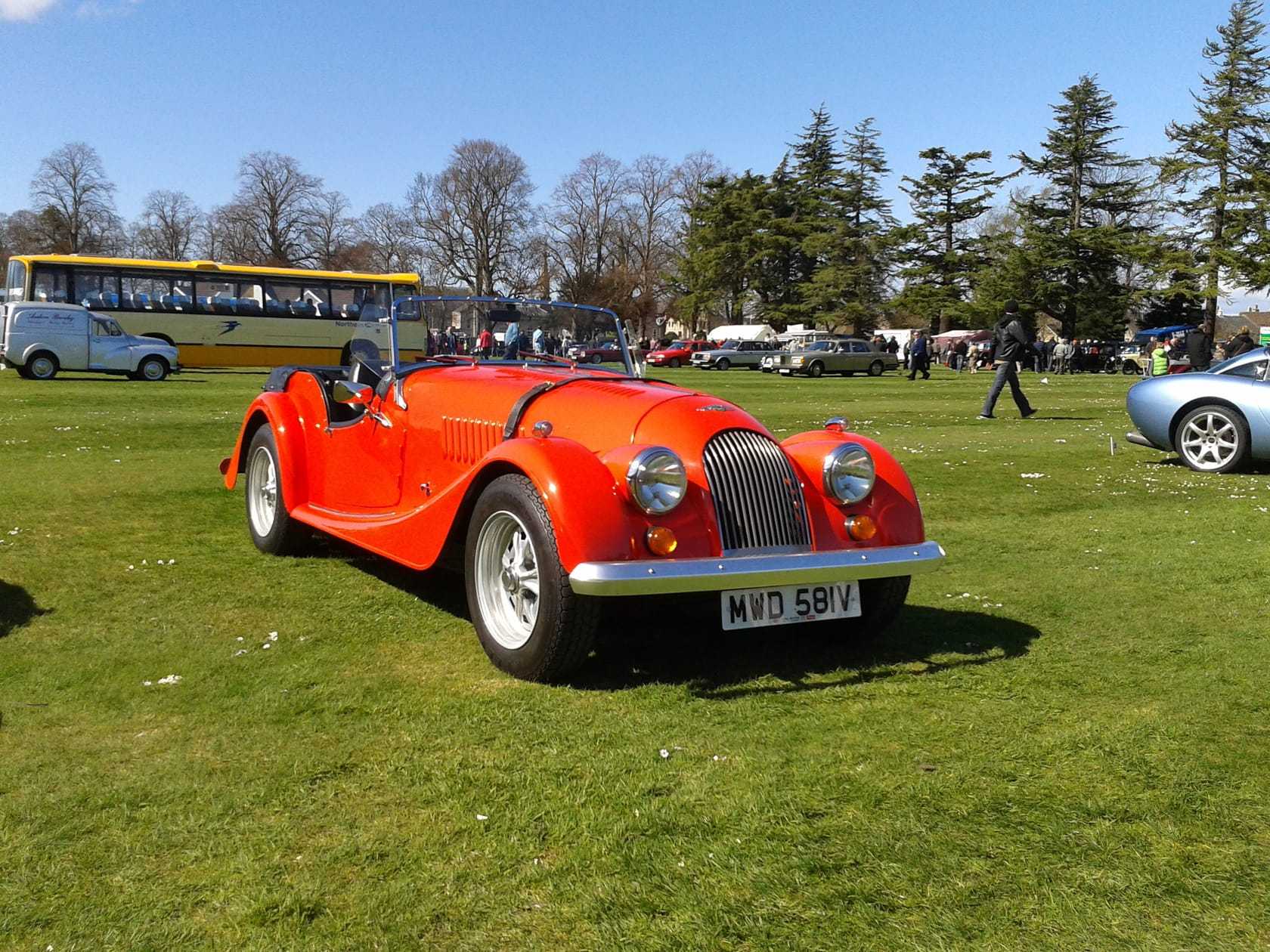 A red 1980 Morgan 4/4 with UK registration NUH 58V on a show field, front three-quarter view