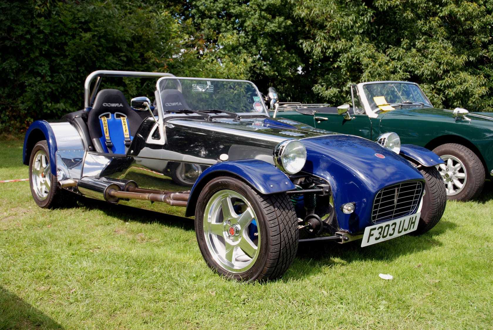 A blue and silver Robin Hood 2B Plus, a Lotus-Seven-style open roadster with a roll bar, front three-quarter view on grass