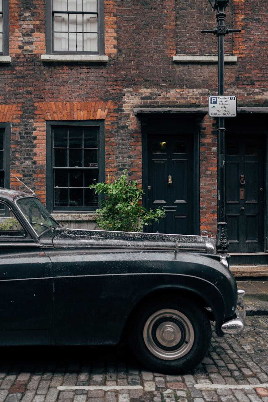 A black classic British saloon with chrome bumpers parked at the kerb outside a brick terrace on a London street