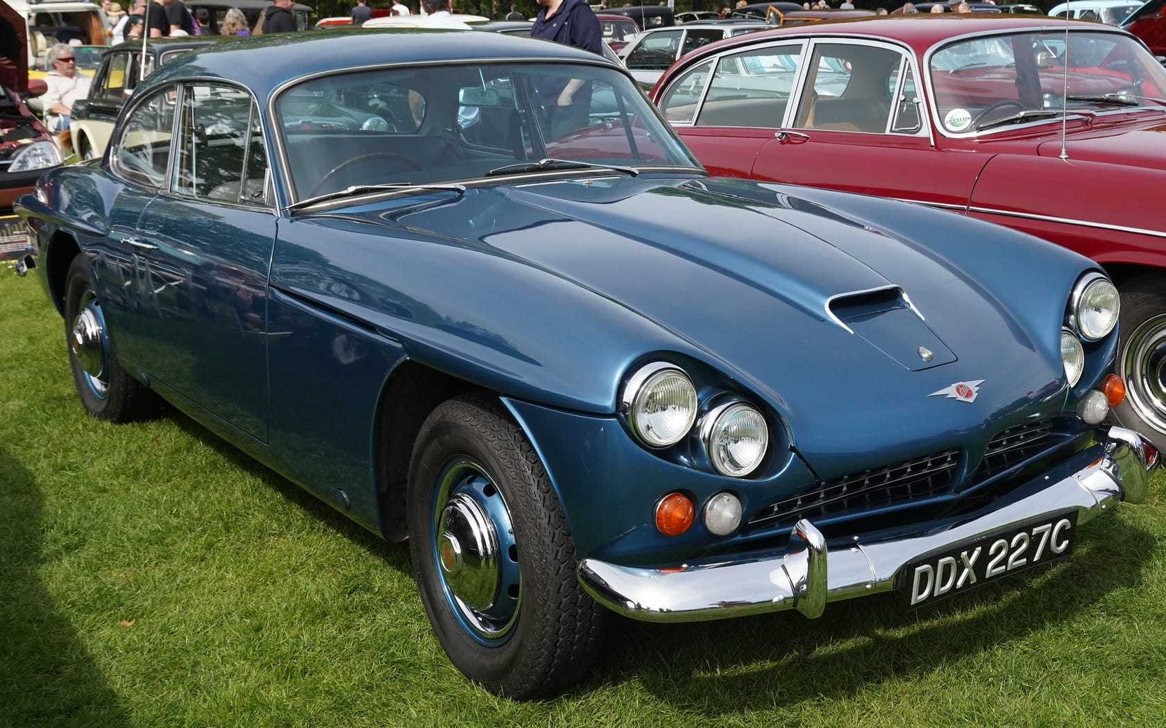 A blue Jensen CV8 Mk III on grass at a show, front three-quarter view, UK registration DDX 227C