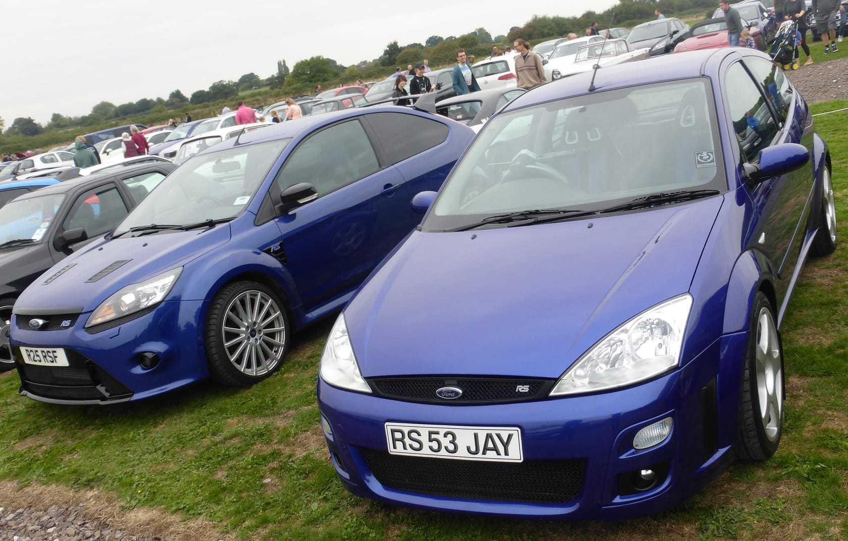An Imperial Blue 2003 Ford Focus RS Mk1 with a UK registration on a show field, a blue Mk2 RS behind it
