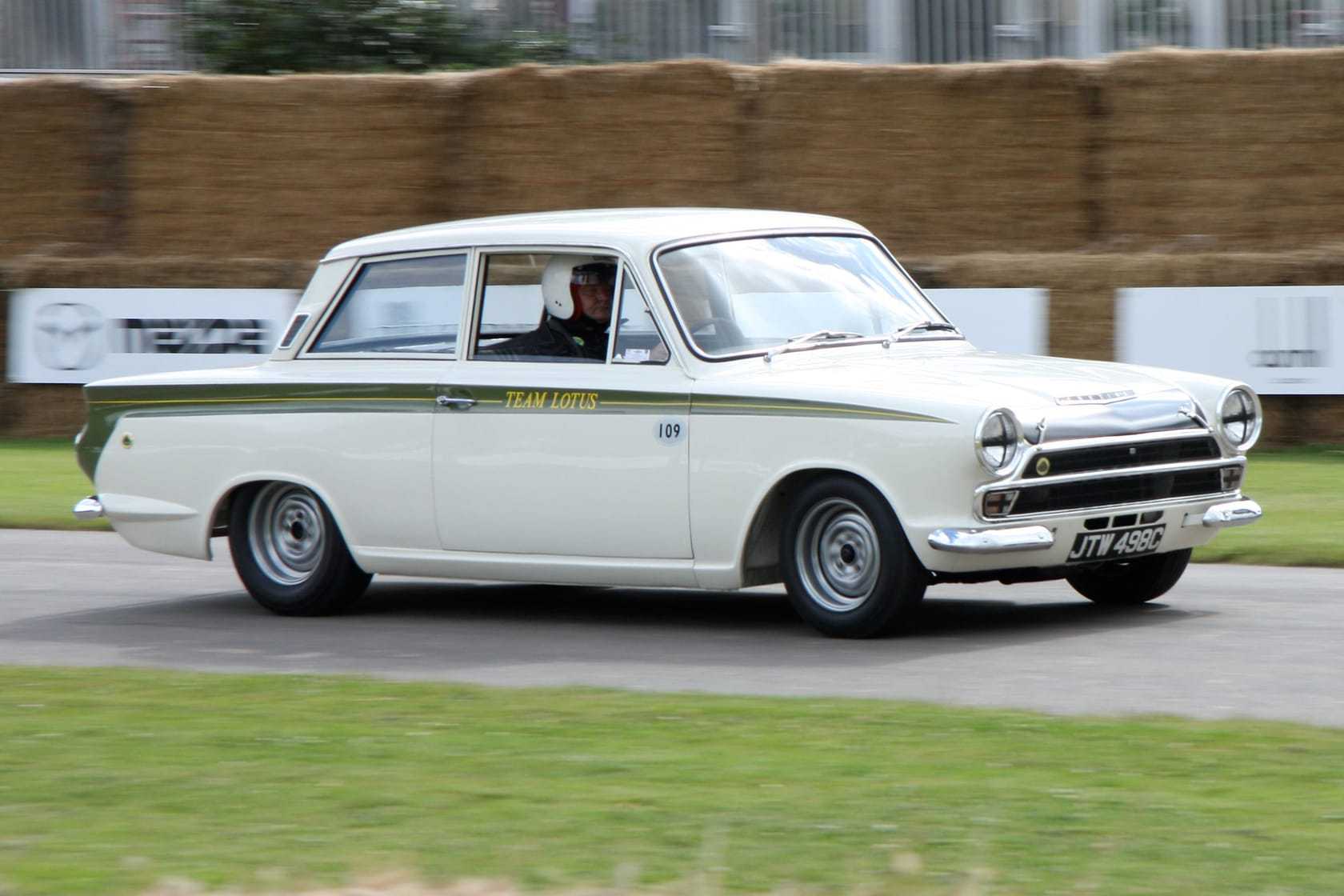 A white Ford Lotus Cortina Mk1 with a green side flash, number 109 and Team Lotus lettering, cornering at the Goodwood Festival of Speed