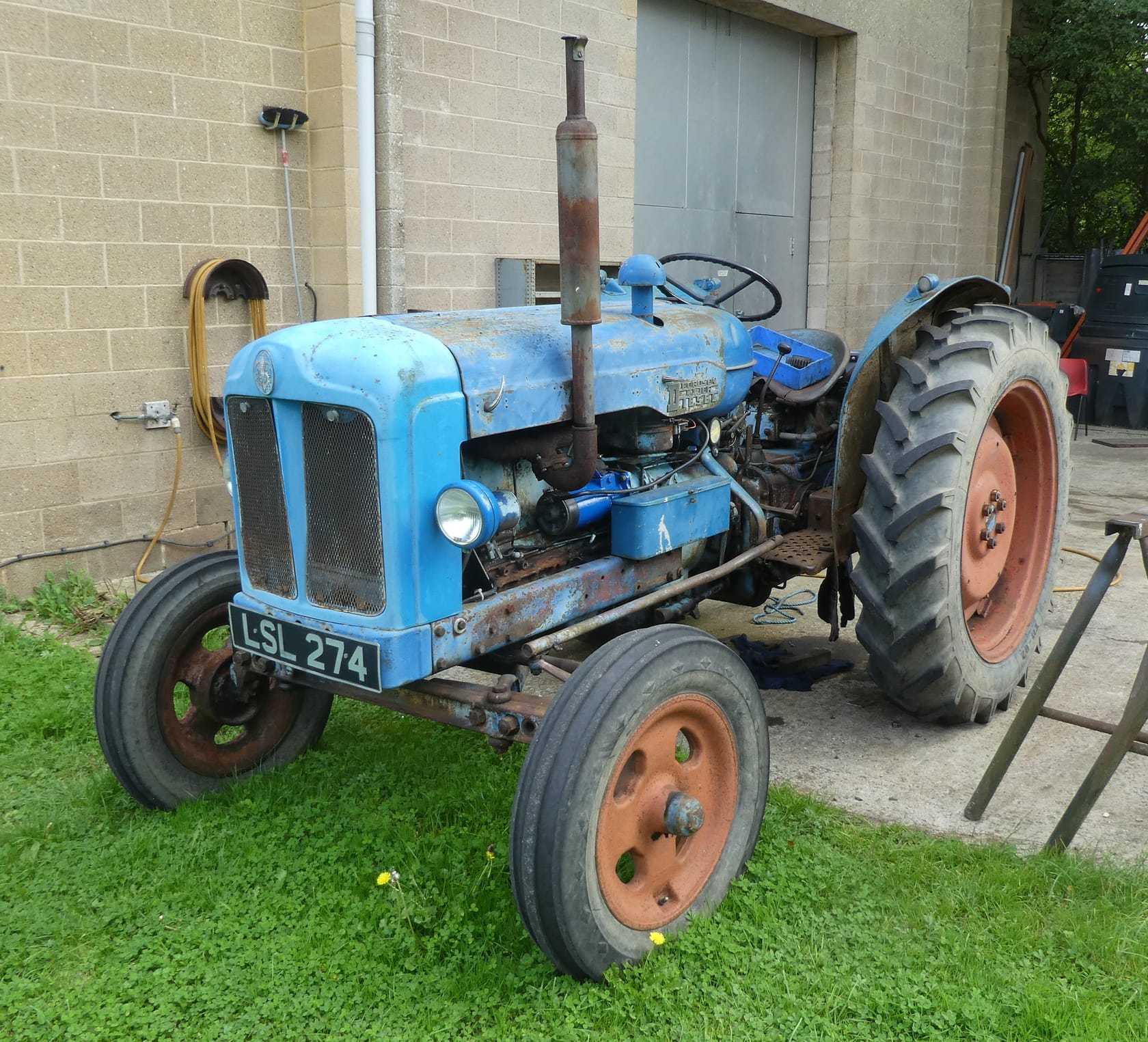 A blue 1952 Fordson Major Diesel tractor, front three-quarter view with an upright exhaust, parked by a workshop