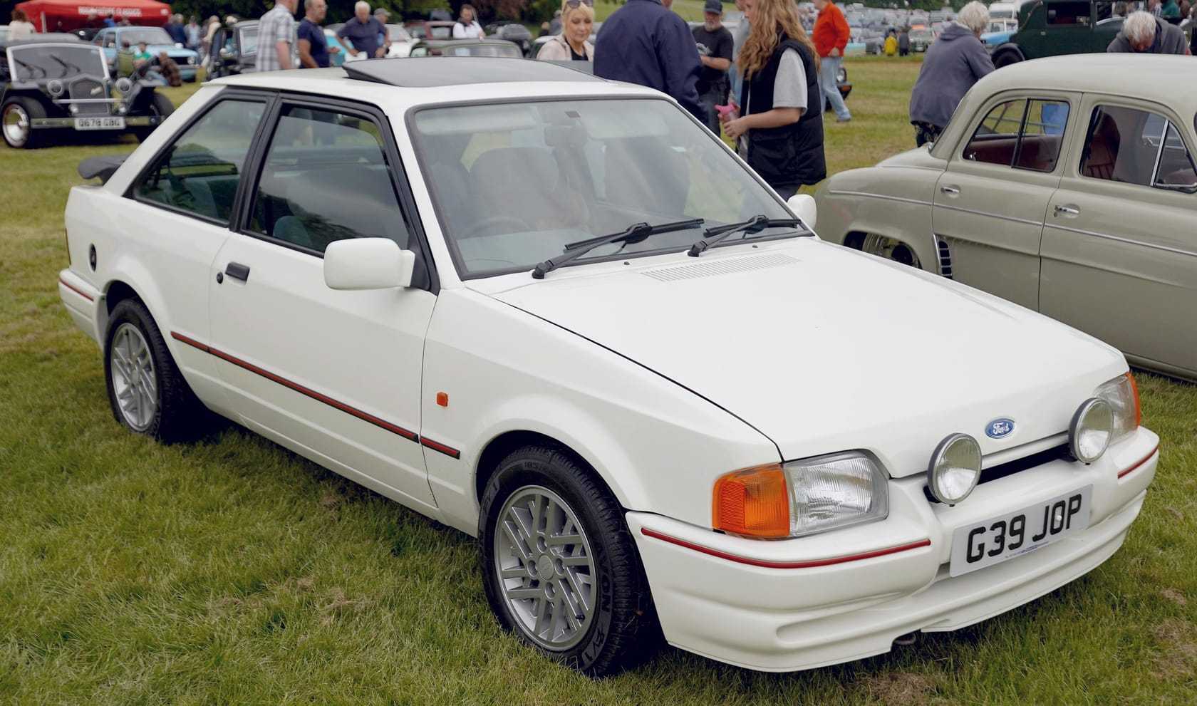 A white Ford Escort XR3i hatchback with a sunroof open, front three-quarter view at a show