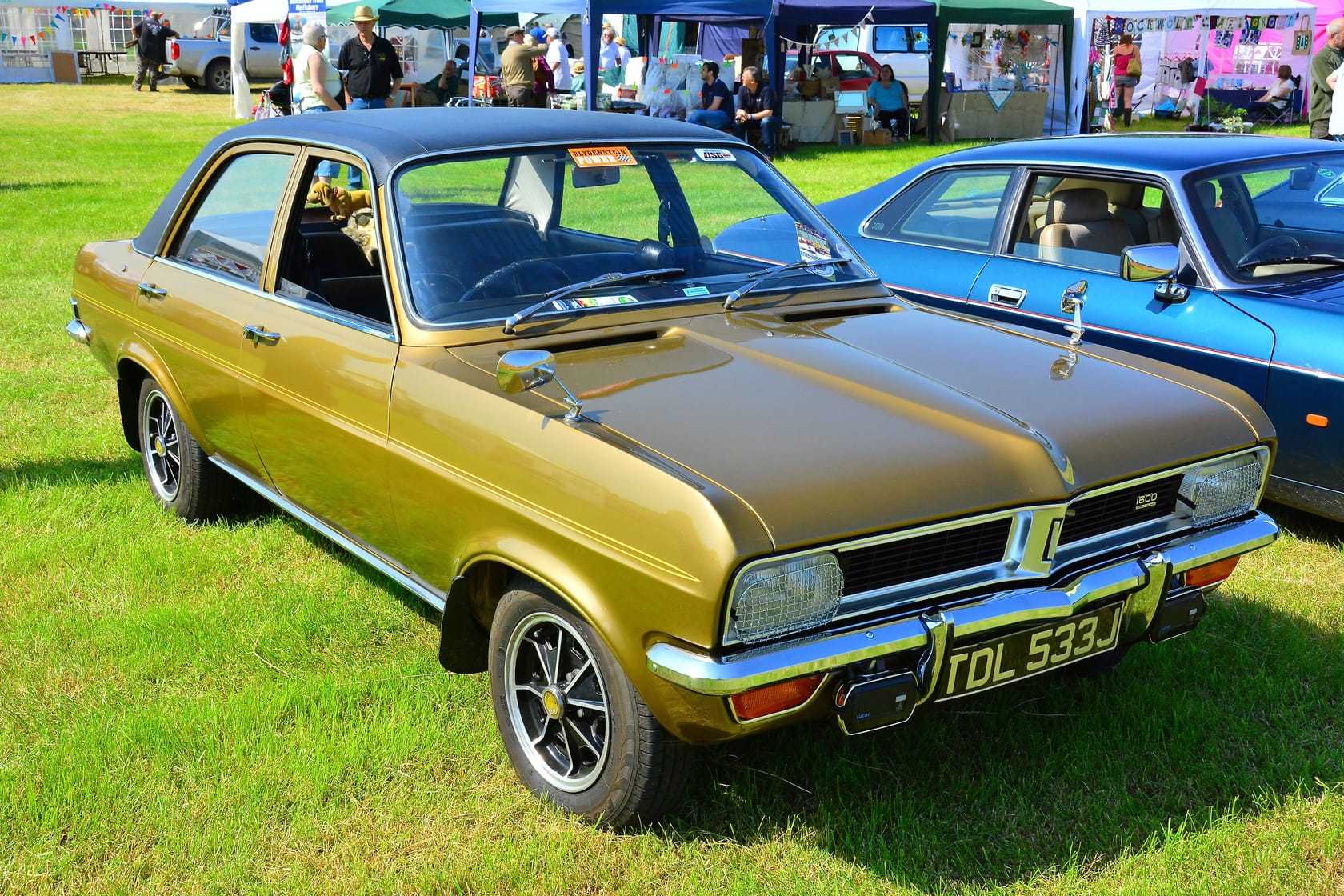 A gold Vauxhall Viva HB with black Brabham-style bonnet stripes at a country fair, front three-quarter view, UK registration TDL 533J