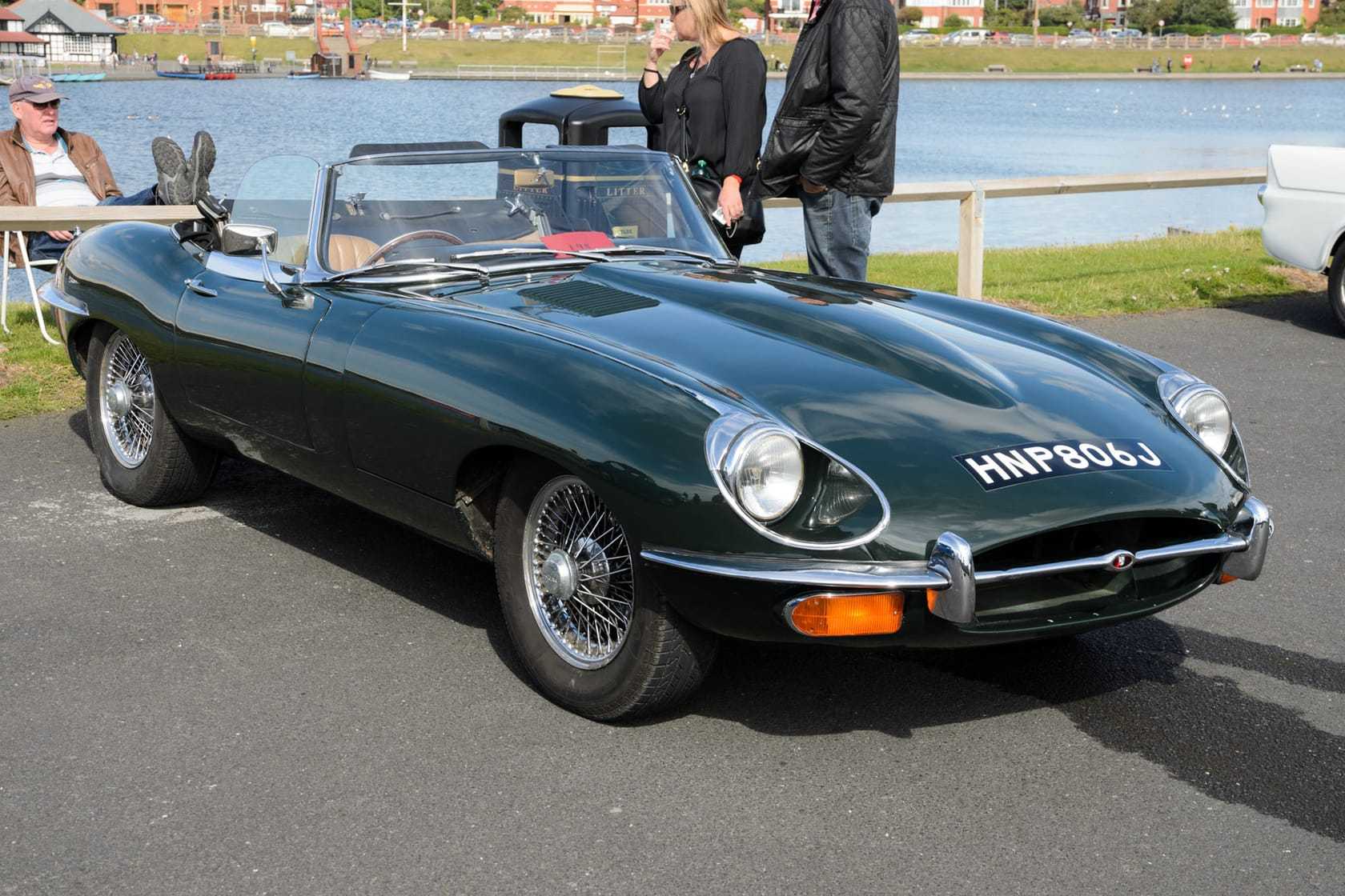 A dark green 1970 Jaguar E-Type Series 2 roadster with UK registration HNP 806J parked by a waterfront
