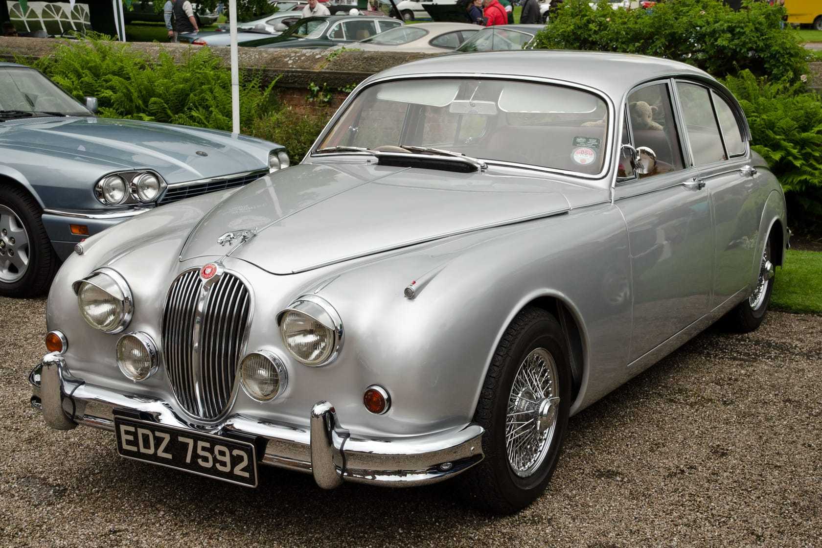 A silver 1964 Jaguar Mk2 saloon with wire wheels parked on grass at a classic car show
