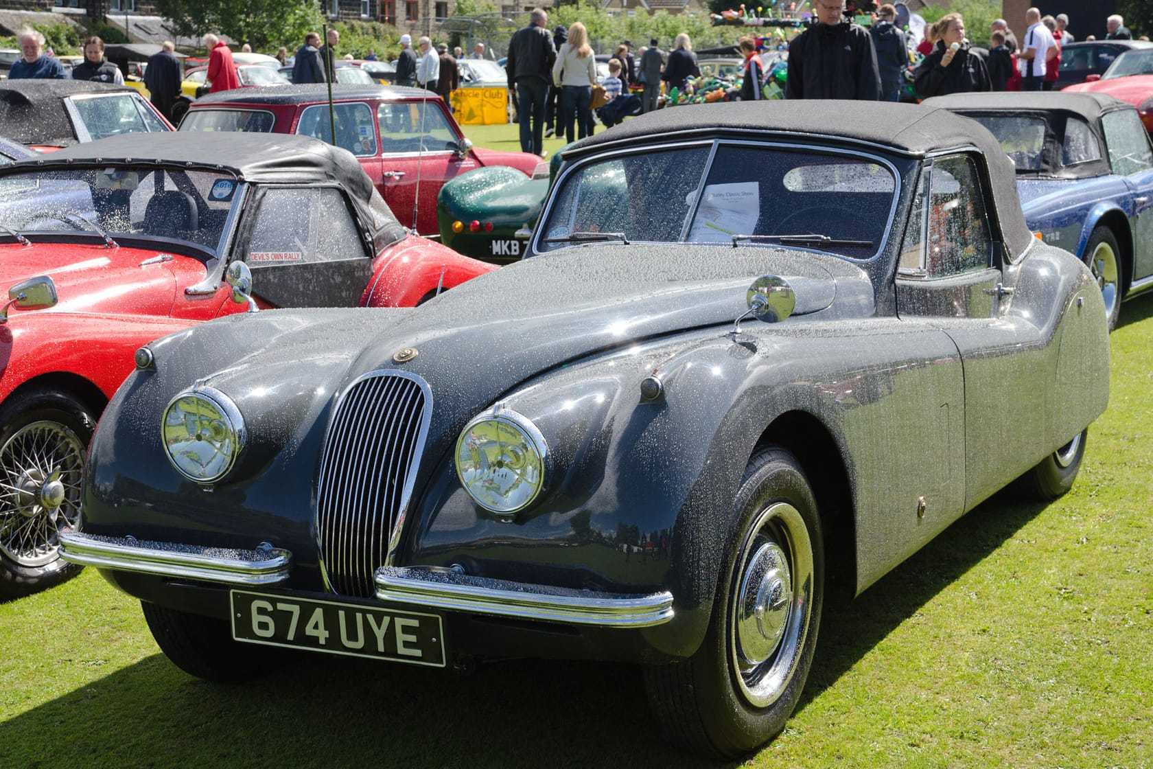 A grey 1953 Jaguar XK120 drophead coupé with a UK registration on a crowded show field