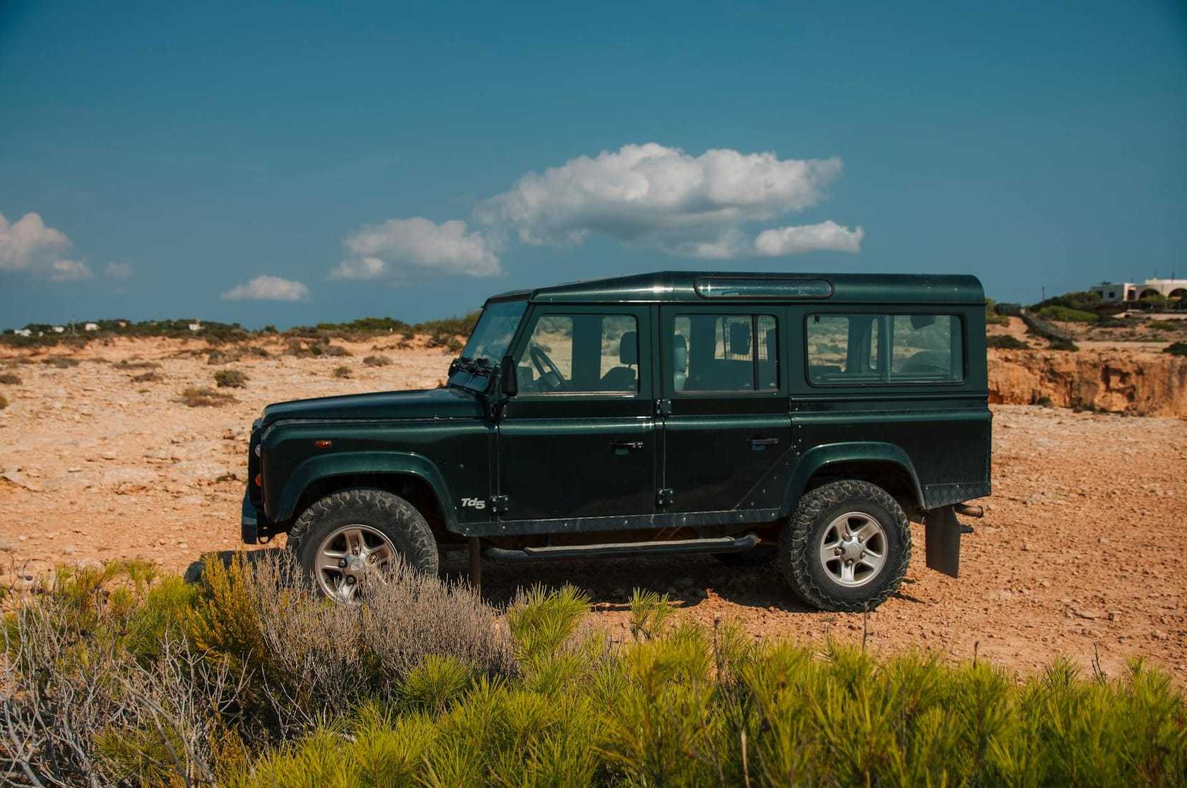 A green Land Rover Defender 110 parked on open scrubland under a blue sky