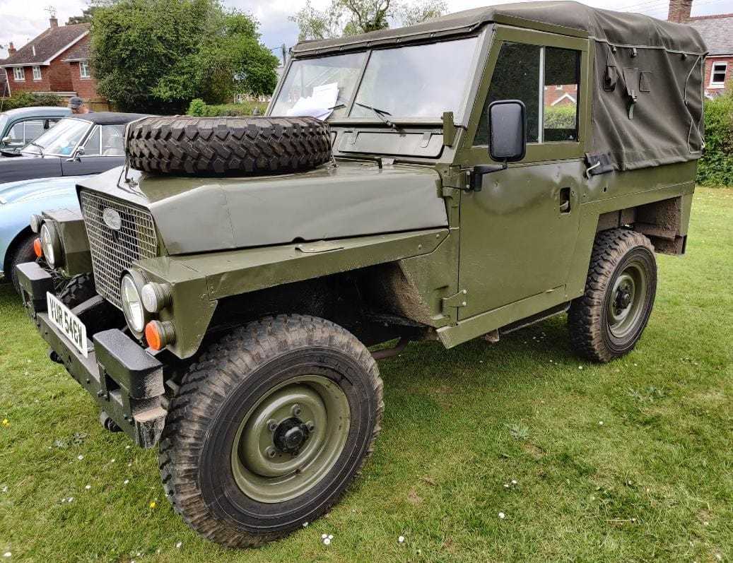 An olive green 1981 Land Rover Lightweight with a spare wheel on the bonnet, front three-quarter view