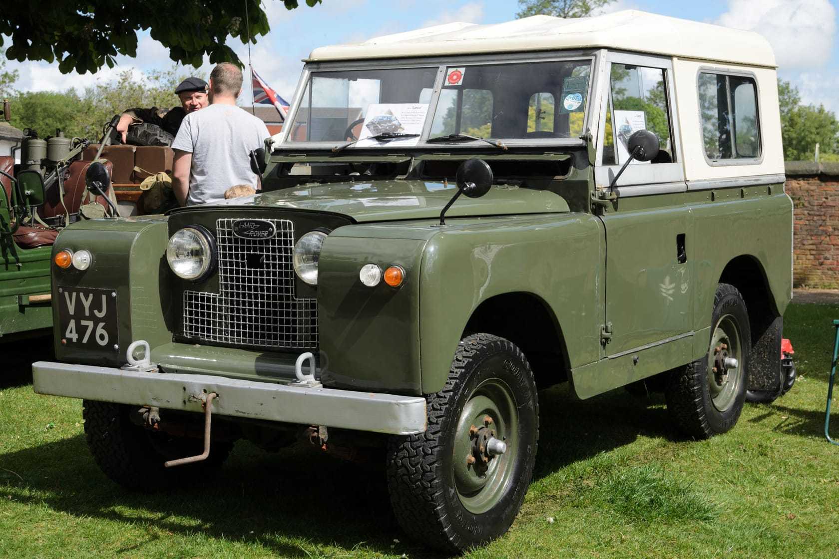 A green 1961 Land Rover Series II 88 with a white roof and a UK registration on a show field