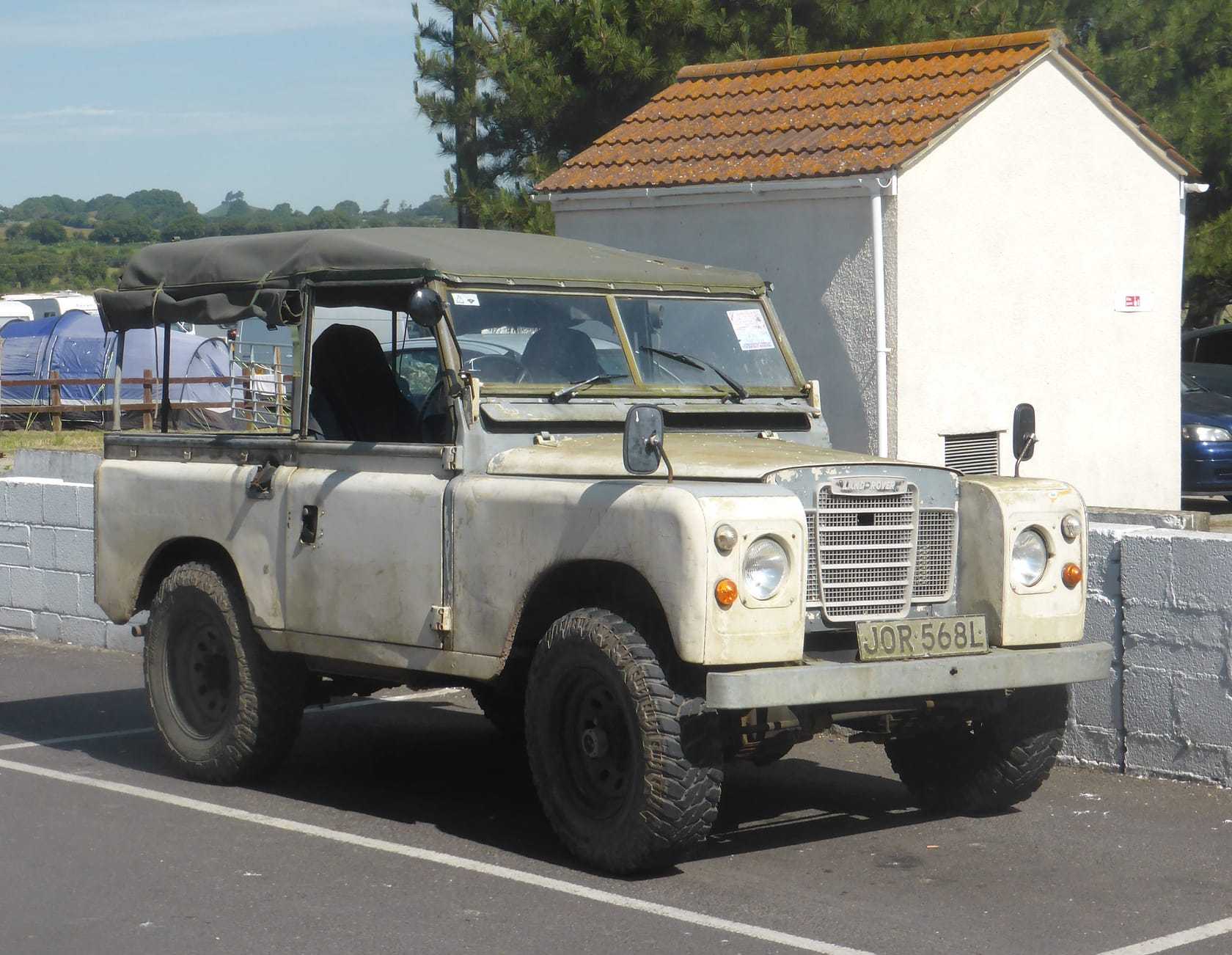 A cream 1972 Land Rover Series III 88 soft-top with a UK registration parked beside a stone wall