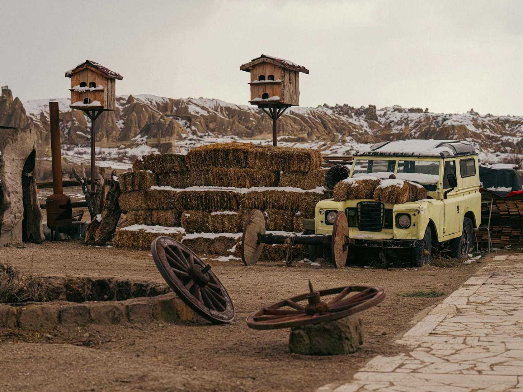 A yellow Land Rover Series III parked among hay bales in a wintry yard