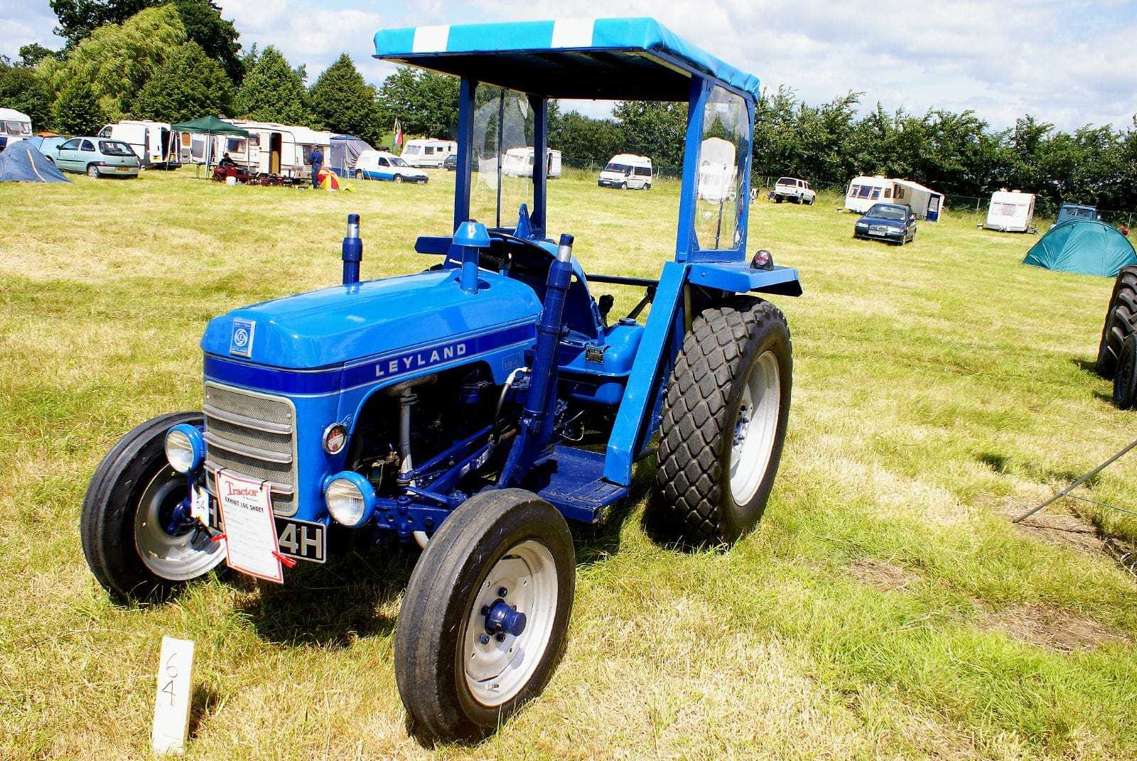 A two-tone blue Leyland 154 compact tractor with a safety canopy, parked on grass at a vintage show