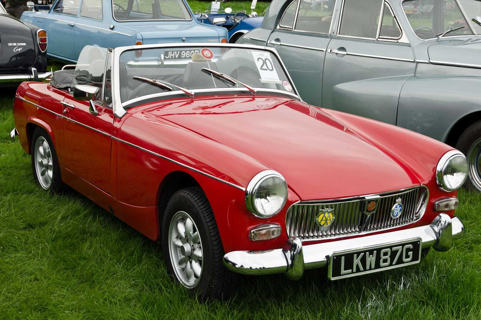 A red 1968 MG Midget Mk III with a UK registration on a show field, its hood down