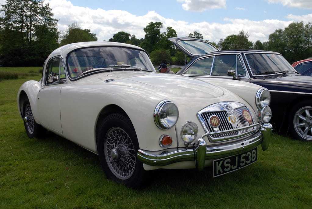 A cream MG MGA fixed-head coupe with wire wheels, front three-quarter view on grass at a classic car show