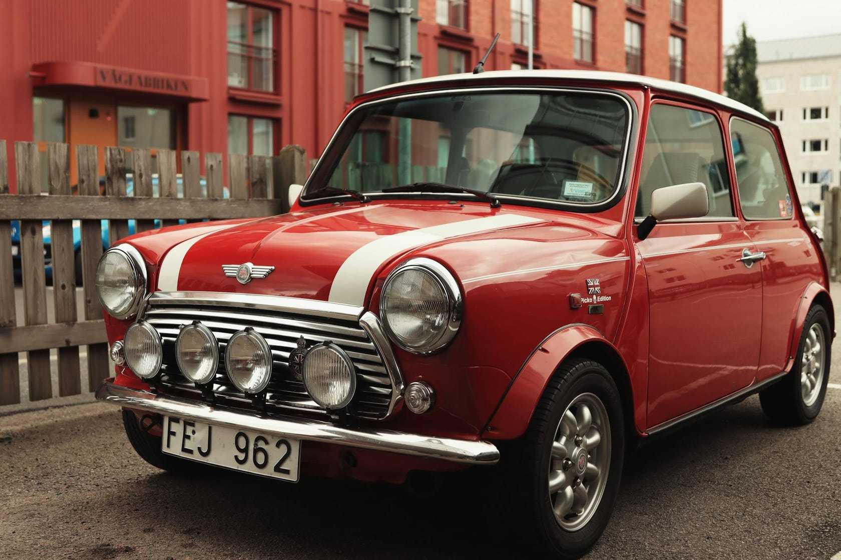 A red Mini Cooper with a white roof and driving lamps, front three-quarter view