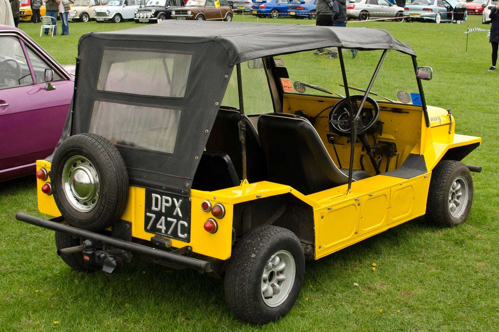 A yellow early British Mini Moke with a canvas top at a show, side view