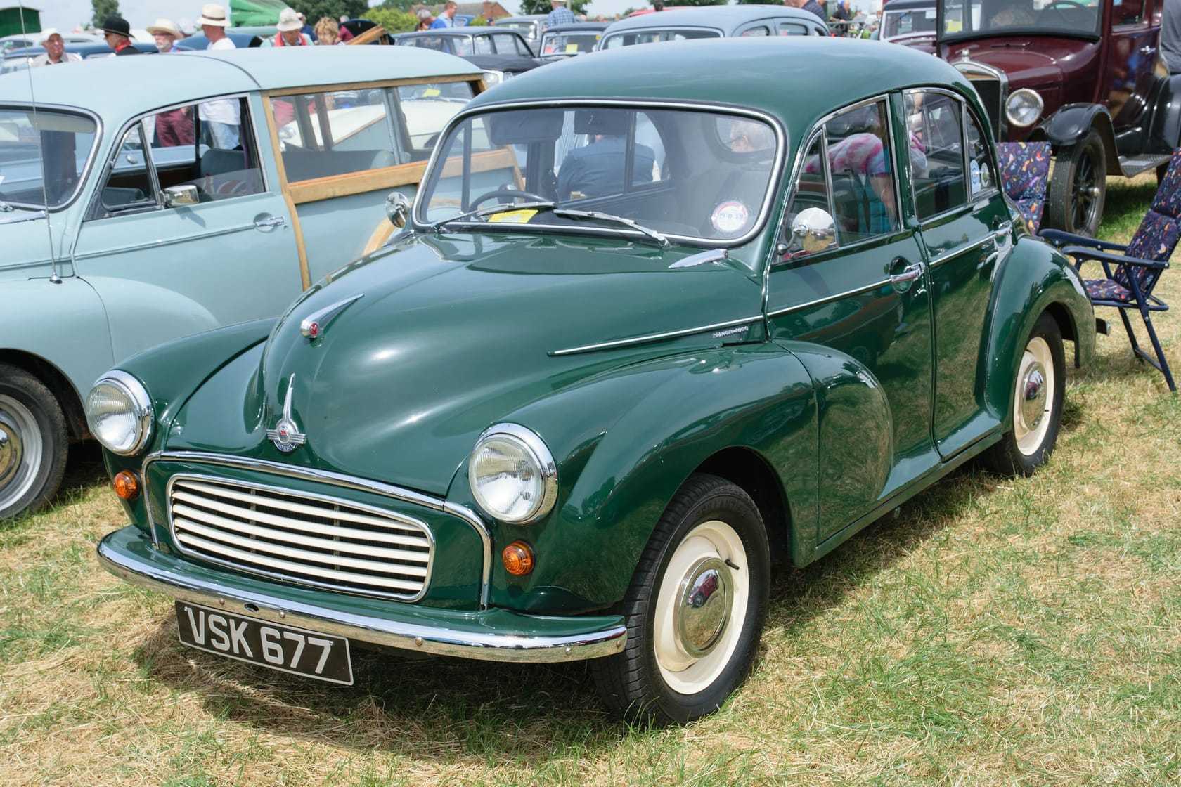 A dark green 1959 Morris Minor 1000 four-door saloon with a UK registration, parked on grass at a show