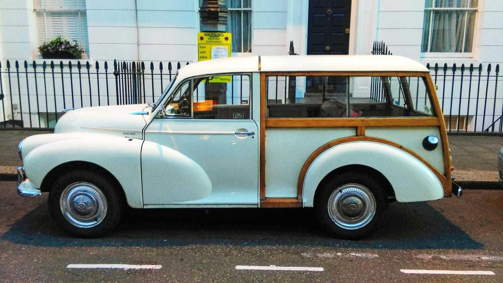 A pale Morris Minor Traveller with timber-framed rear bodywork, parked at the kerb on a London street of white stucco houses