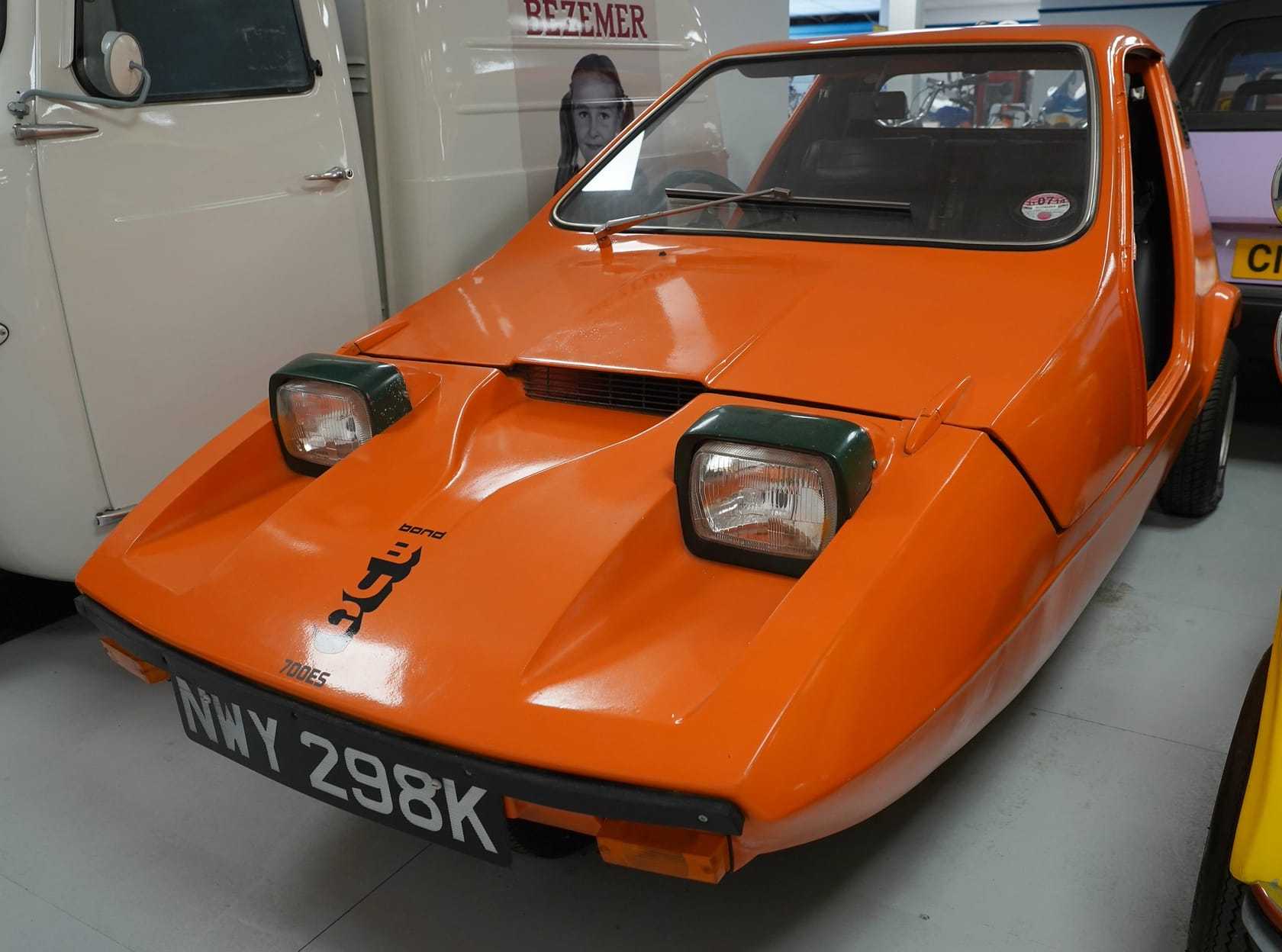 The front of an orange Bond Bug 700ES showing the twin rectangular headlamps with green covers and the Bond badge on the pointed nose