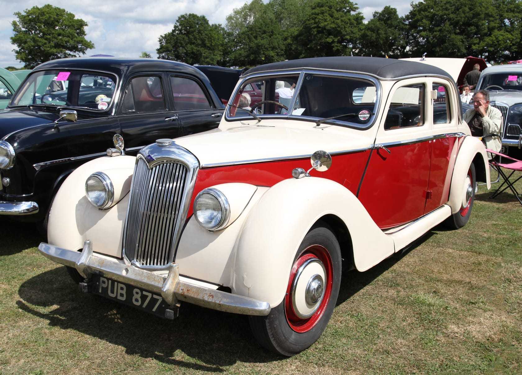 A cream and red Riley RME saloon of the early 1950s parked on grass at a classic car show alongside other classics
