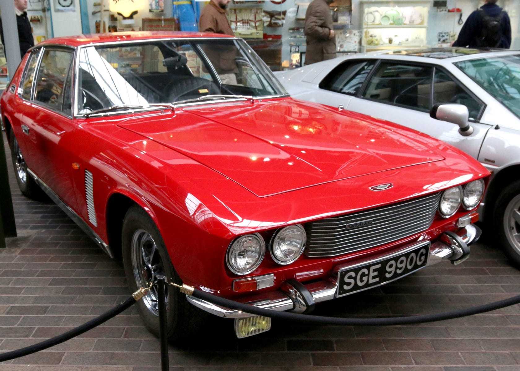 A red Jensen Interceptor at an indoor display, front three-quarter view, UK registration SGE 990G