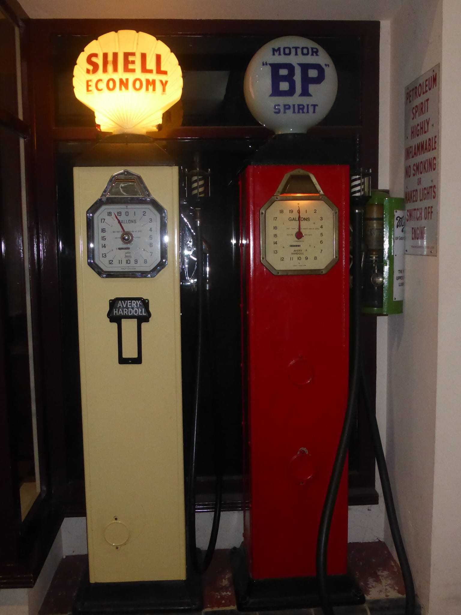 Two restored vintage petrol pumps, one cream Shell Economy and one red BP Motor Spirit, with illuminated glass globes