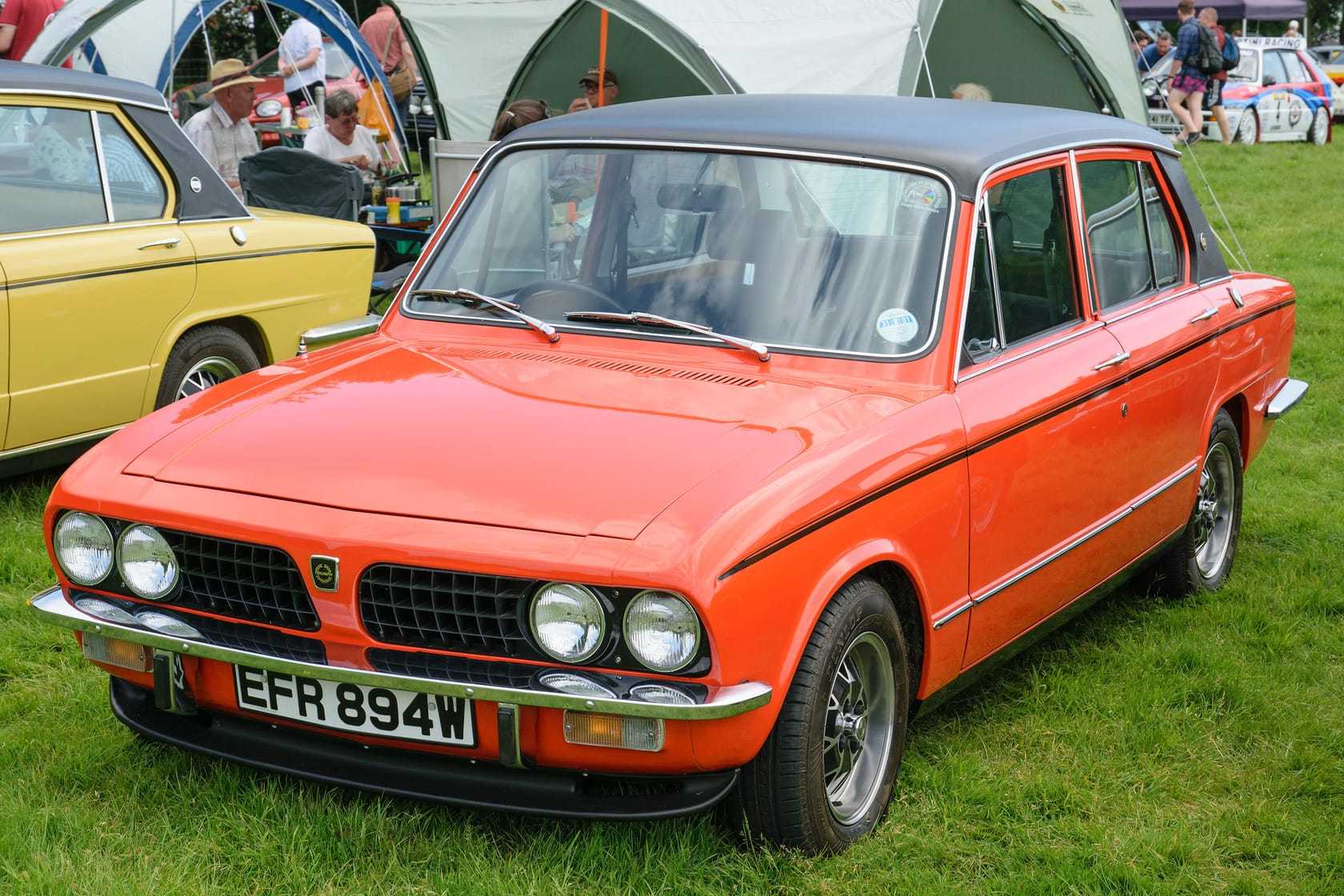 An orange Triumph Dolomite Sprint with a black vinyl roof and alloy wheels, front three-quarter view