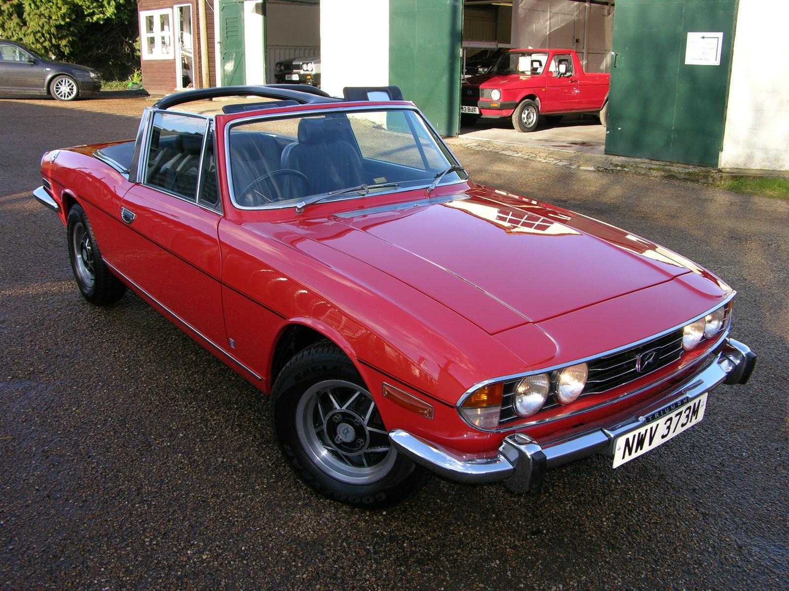 A red Triumph Stag with the top down, showing the T-bar roll hoop, front three-quarter view
