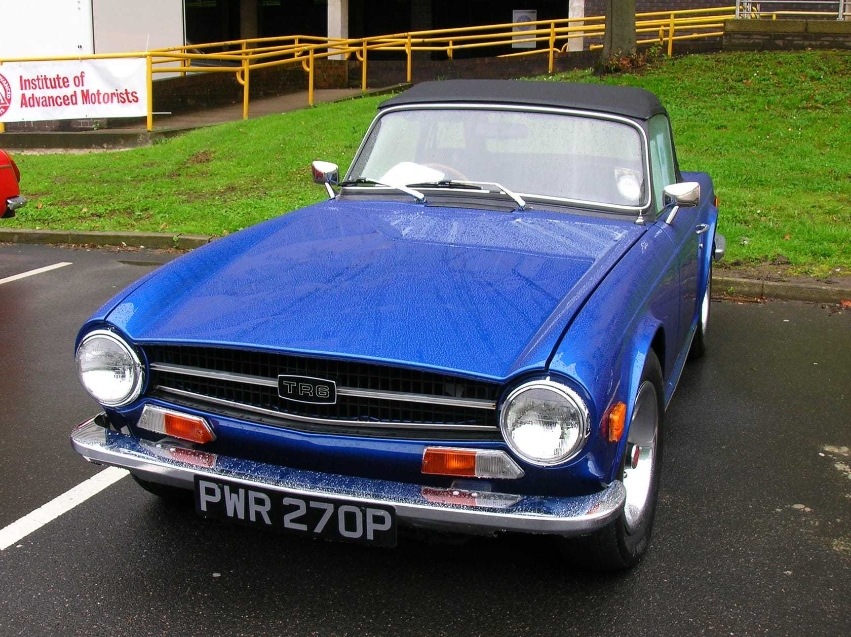 A blue Triumph TR6, top down, front three-quarter view on a road