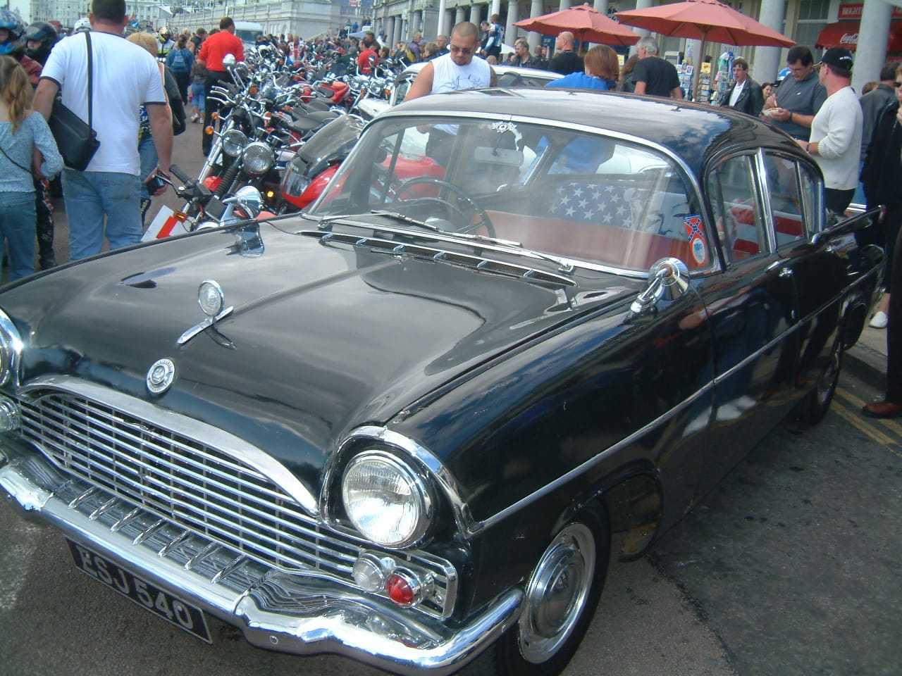 A black Vauxhall saloon with a chrome grille parked among crowds of people and other cars at a busy classic car event