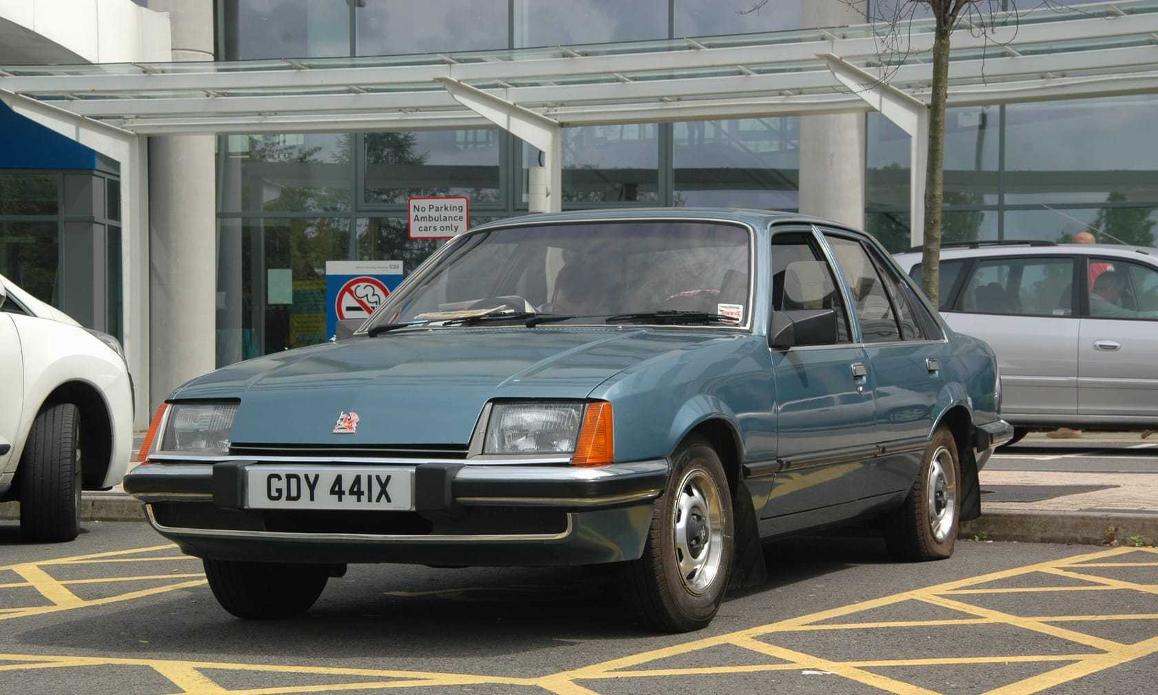 A pale blue early Vauxhall Carlton Mk1 saloon with a 1981 UK registration parked outside a hospital entrance