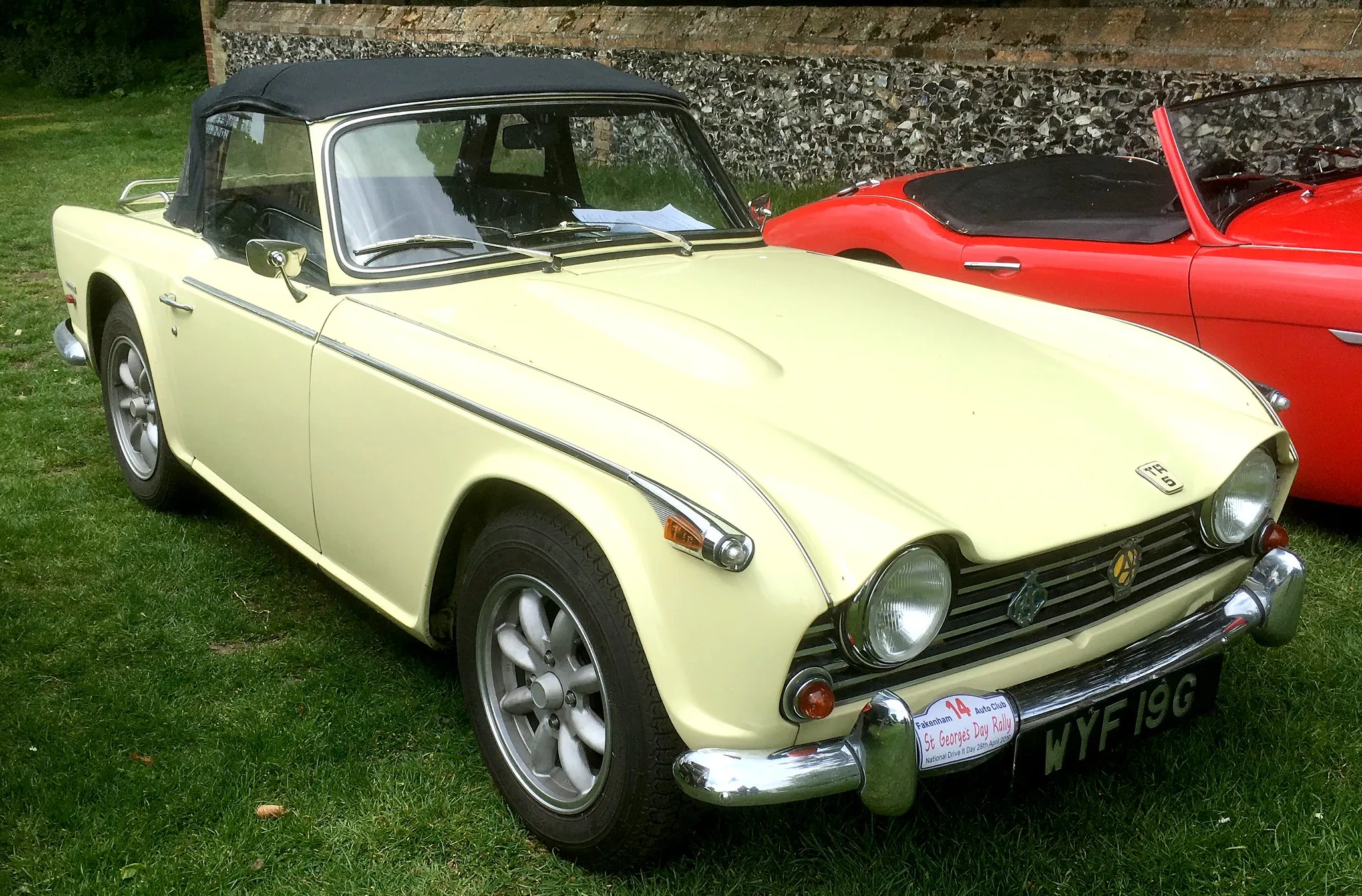 A primrose-yellow Triumph TR5 with a black hardtop, UK registration WYF 19G, front three-quarter view on a show field