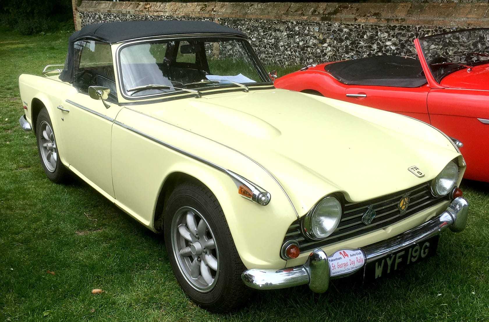 A primrose-yellow Triumph TR5 with a black hardtop, UK registration WYF 19G, front three-quarter view on a show field