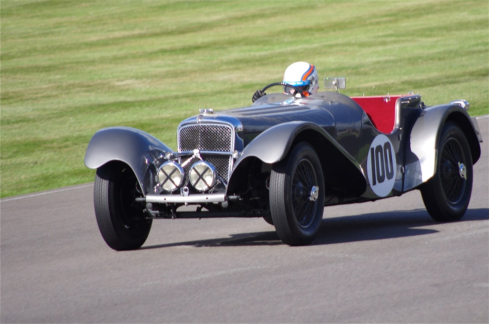 A silver SS Jaguar 100 racing on a circuit, race number 100