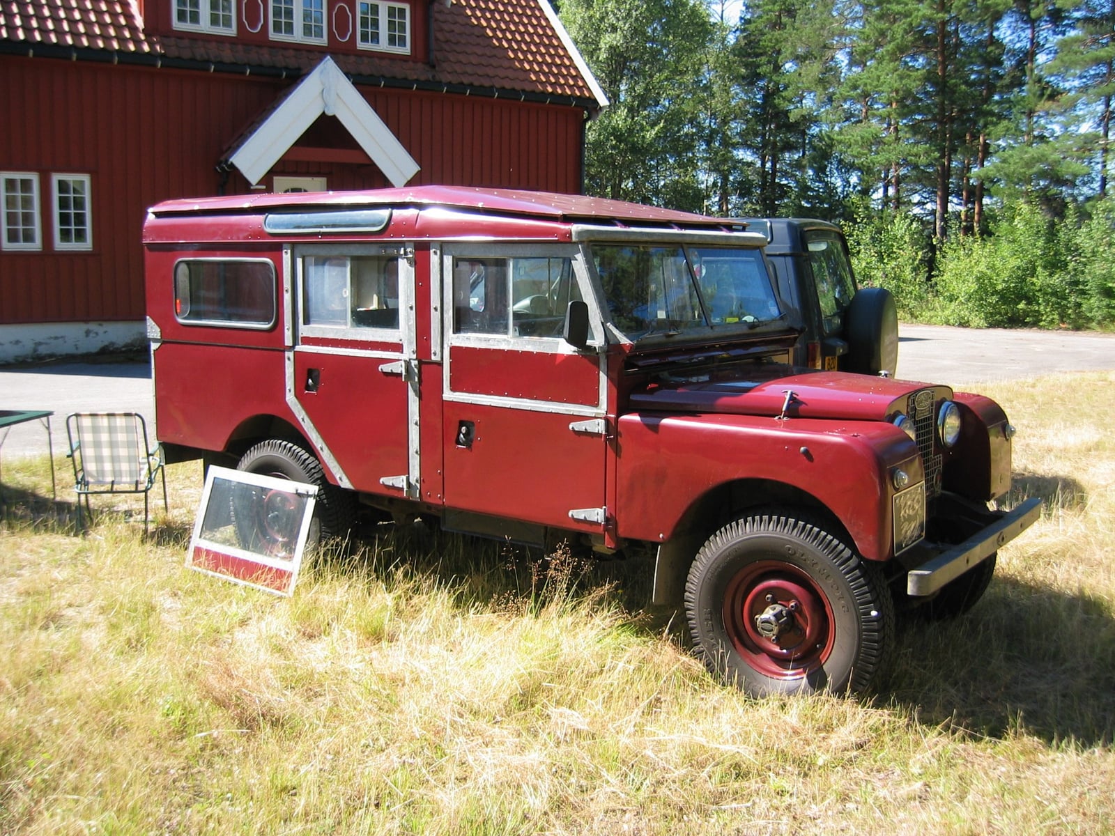 A red Land Rover Series I station wagon, front three-quarter view, its headlamps set behind the grille mesh in the early style