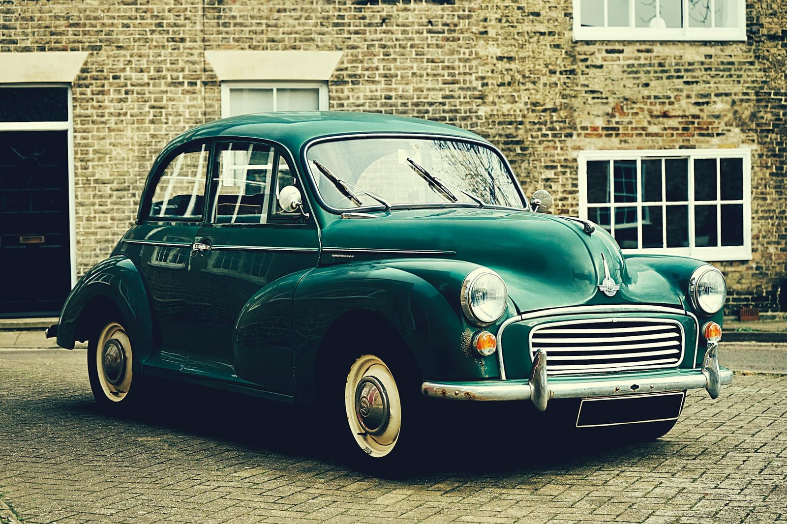 A green Morris Minor saloon parked on cobbles outside a brick building in Ely