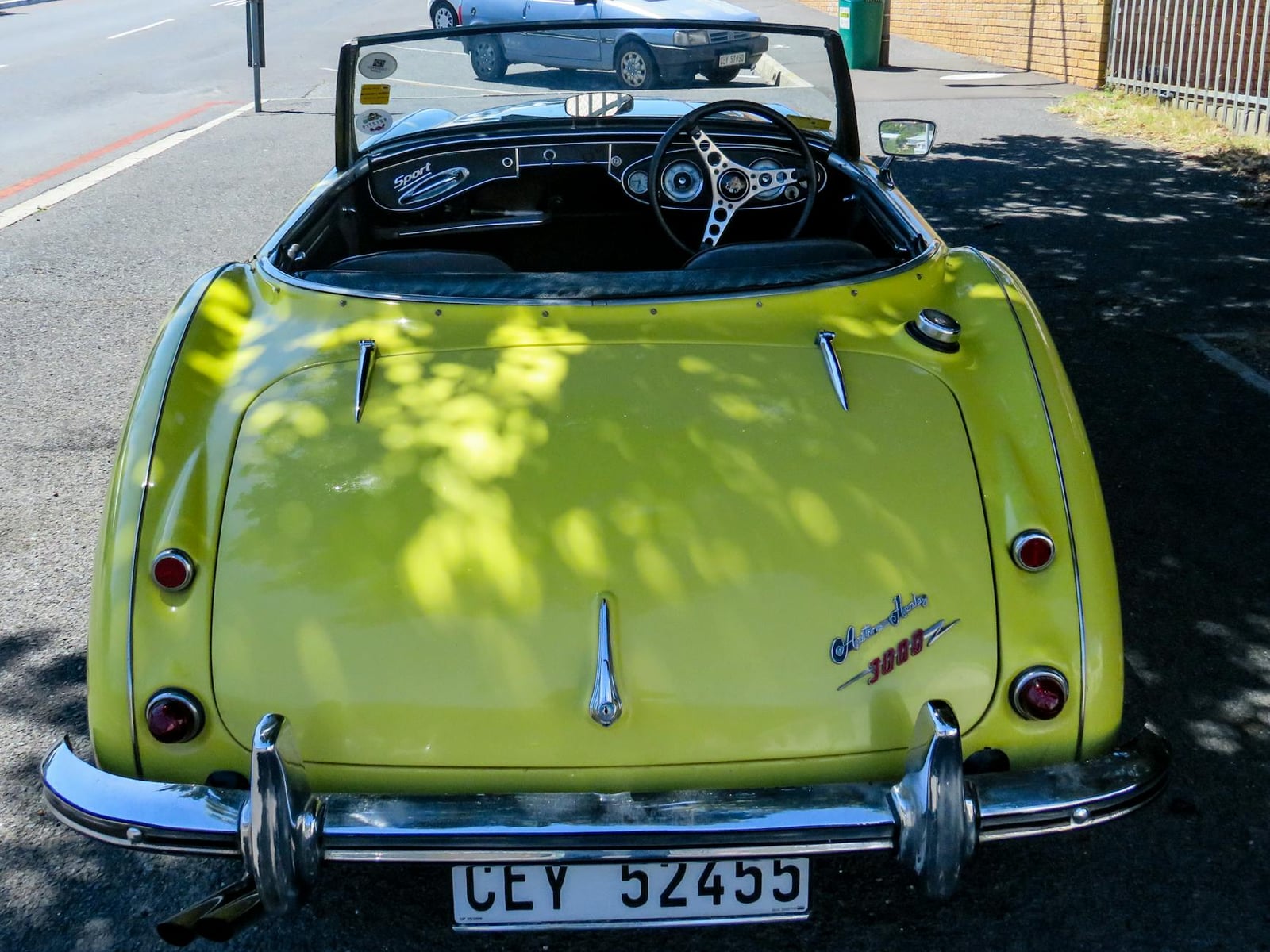 A yellow Austin-Healey 3000 roadster seen from the rear with the hood down
