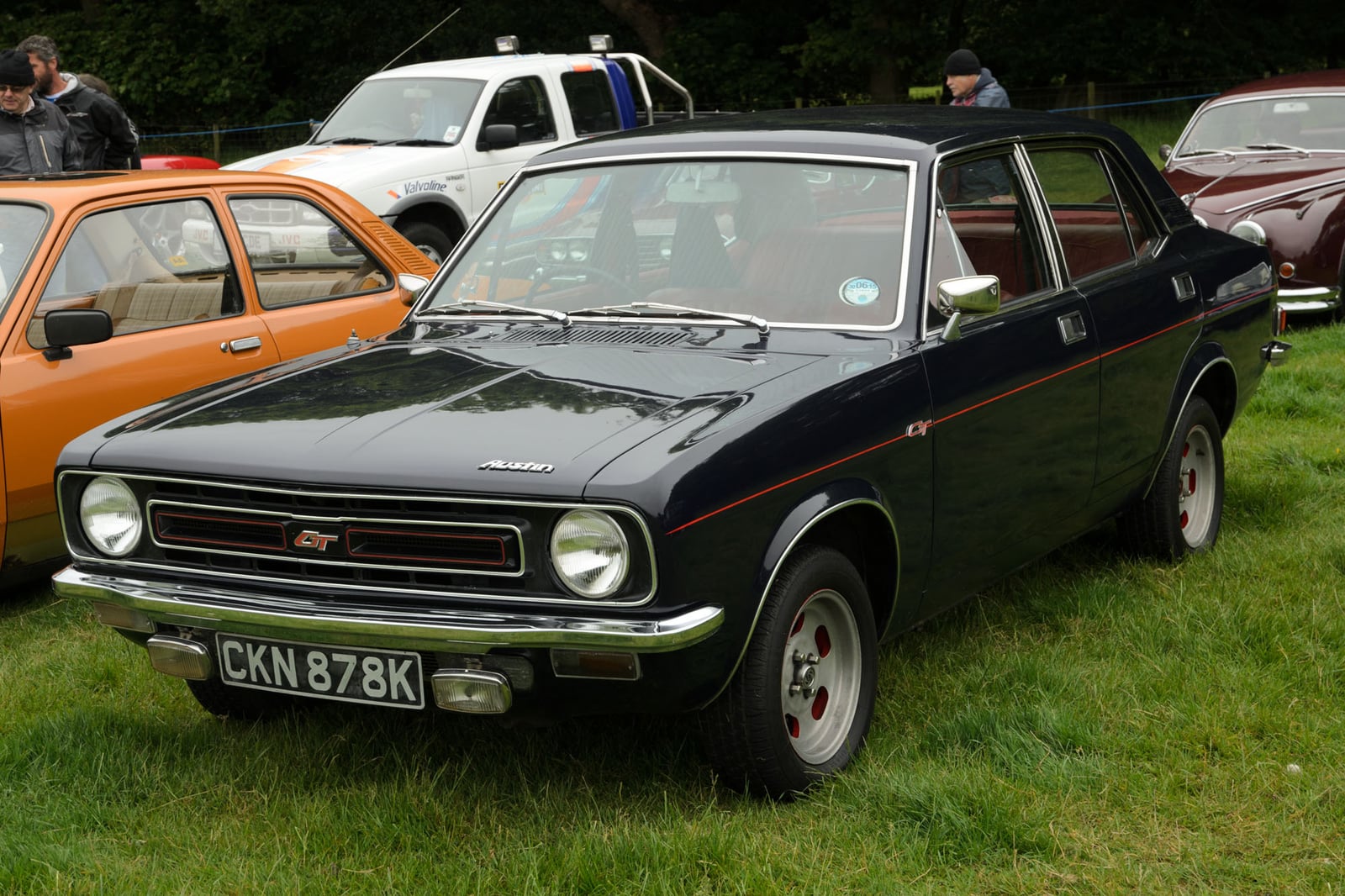 A black 1972 Austin Marina 1.3 GT four-door saloon with red coachline and GT badging, front three-quarter view at a UK classic car show