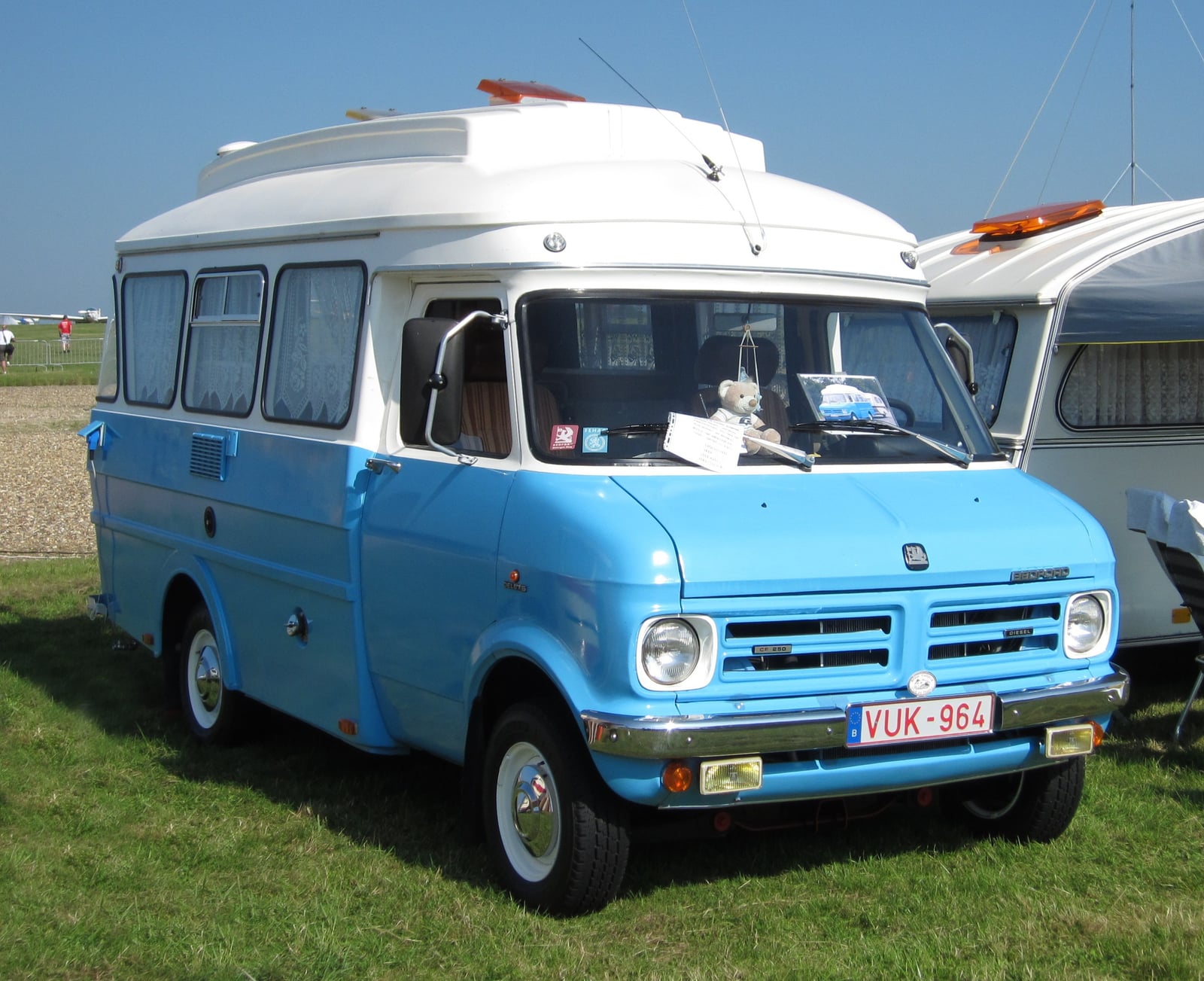 A blue and white Bedford CF Dormobile Debonair high-top campervan on grass at a show, front three-quarter view