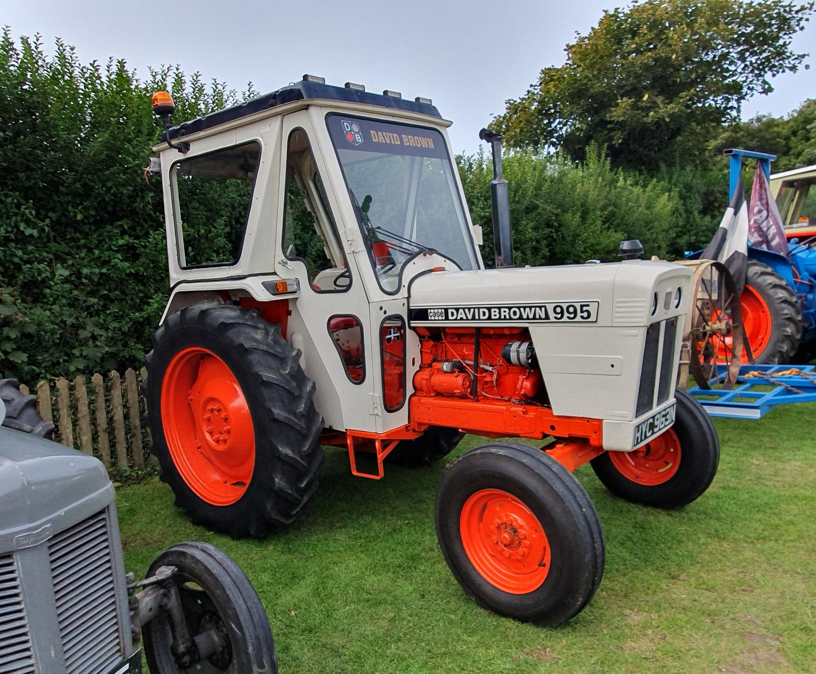 A white David Brown 995 with a cab on grass at a Cornish vintage rally, a grey Ferguson in front