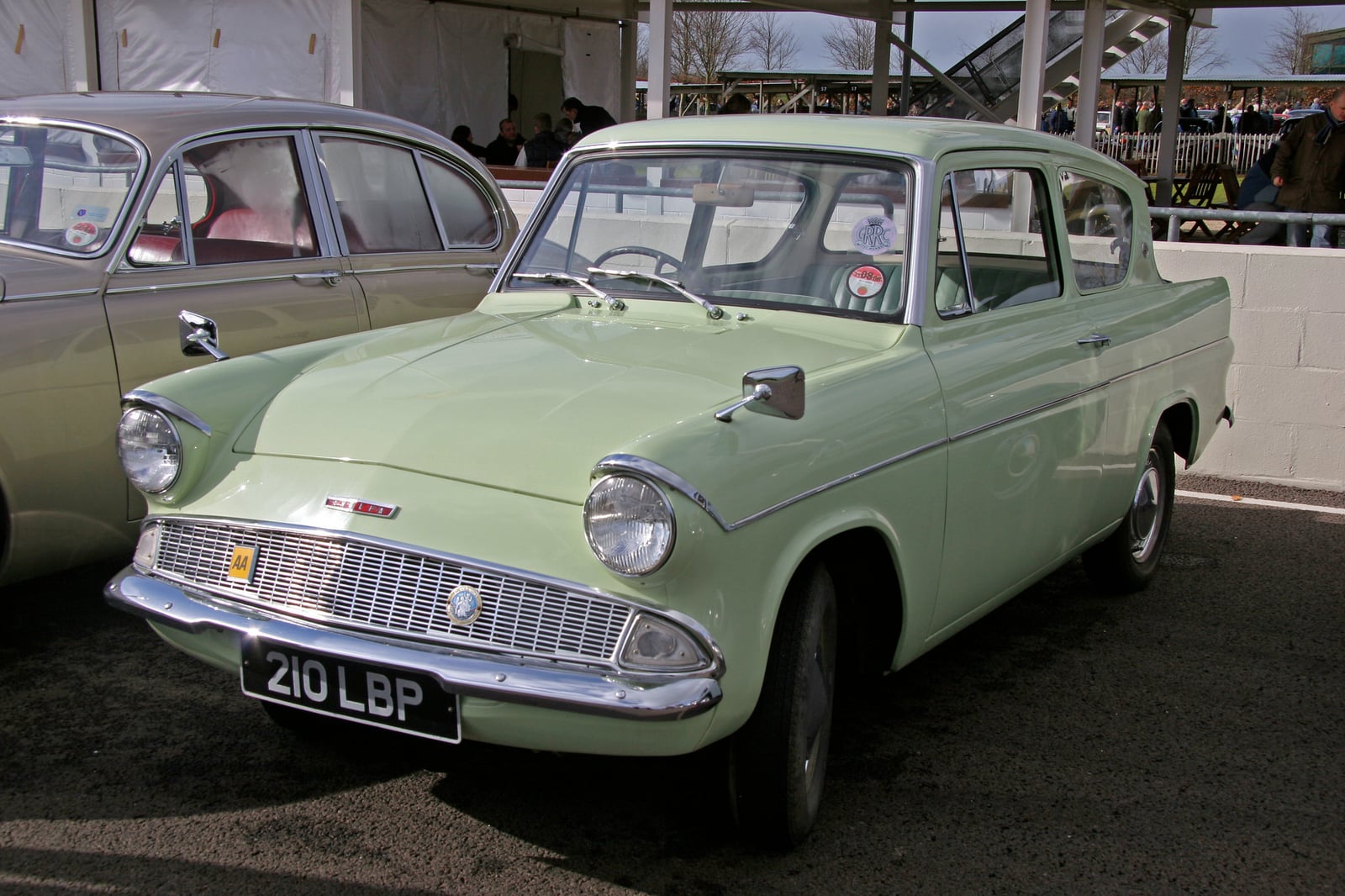 A pale green Ford Anglia 105E Deluxe with its reverse-rake rear window, front three-quarter view at a classic car meeting