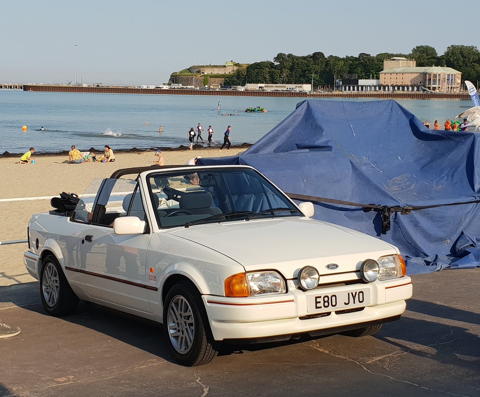 A white Ford Escort XR3i cabriolet on a seafront, front three-quarter view