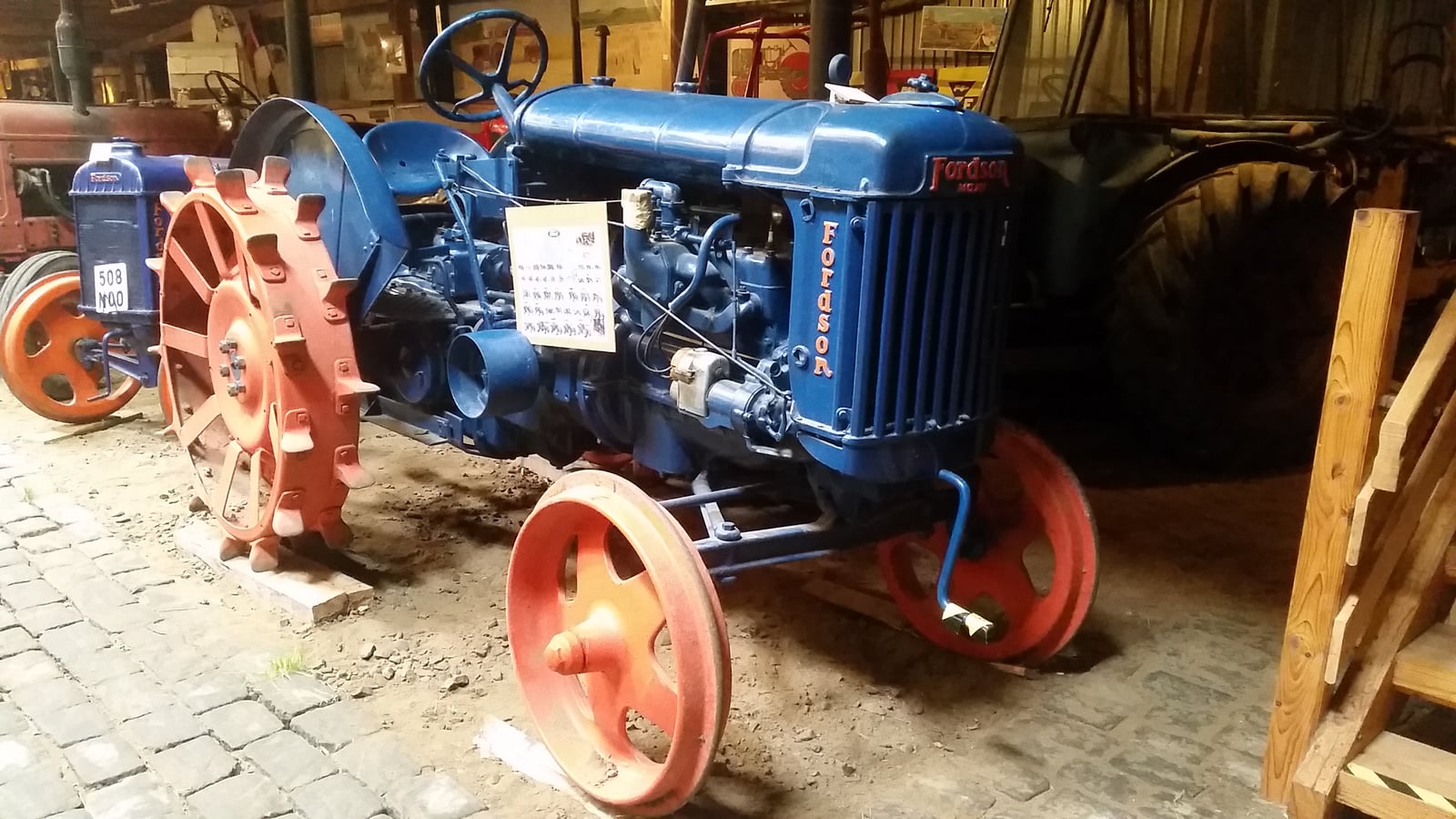 A restored blue Fordson Major E27N tractor with spade-lugged steel rear wheels and red spoked front wheels, on display indoors