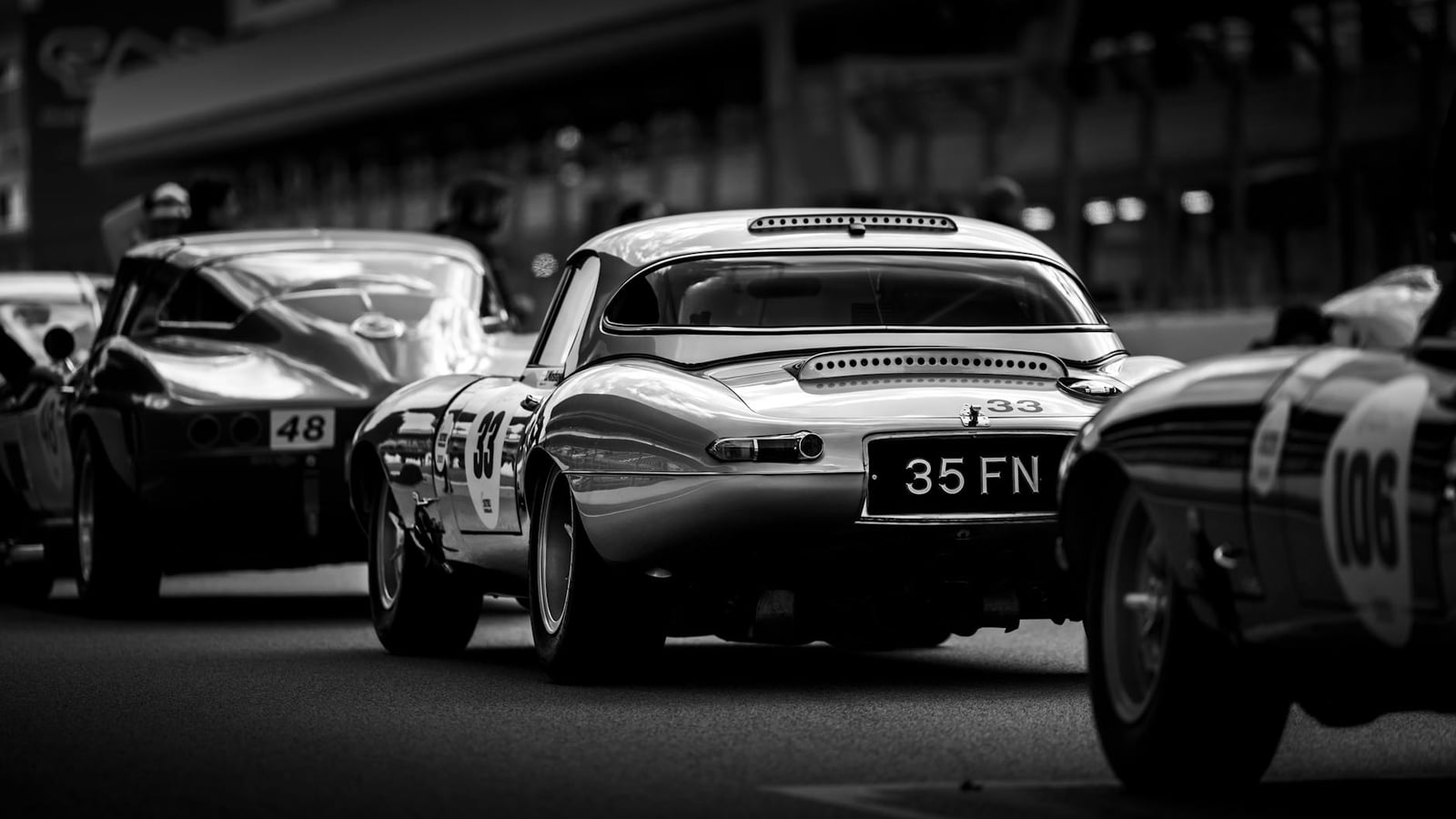 Jaguar E-Type race cars lined up on a circuit, in black and white